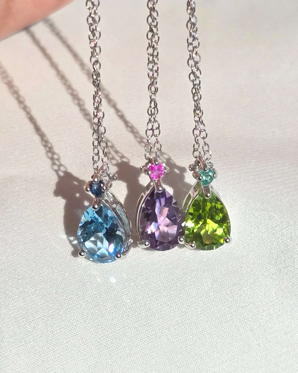 Sterling silver pear-cut gemstone pendant necklace set on display, three colors