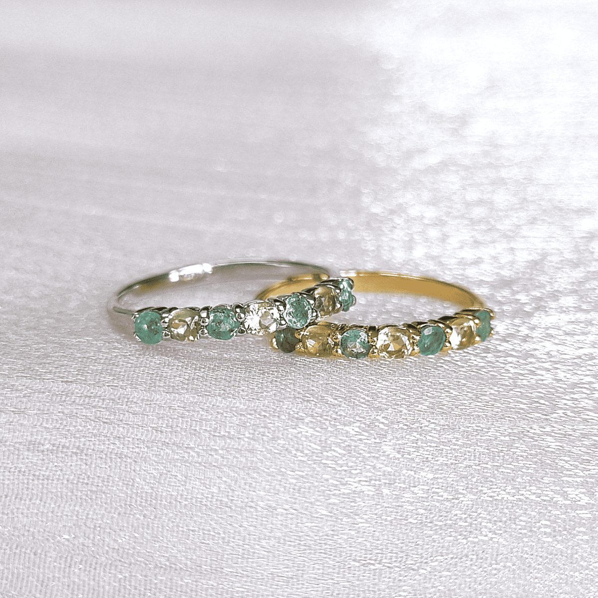 Two rings stacked: sterling silver and gold-toned bands with green gemstones