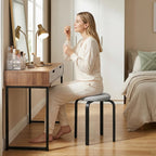 Grey cushioned round backless stool with black legs, used as a dining seat