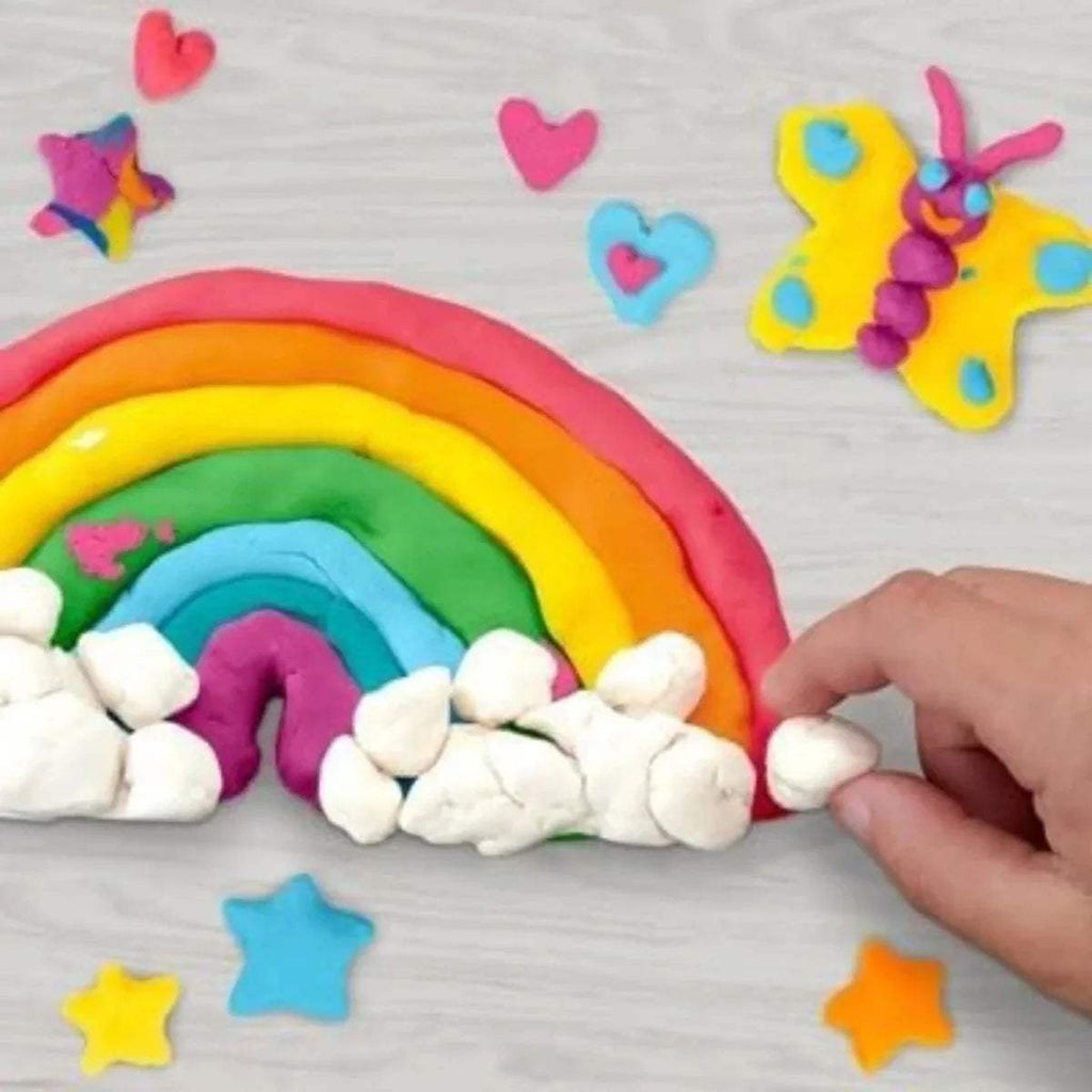 Rainbow modeling clay with white pieces, hearts and stars, and a hand placing pieces