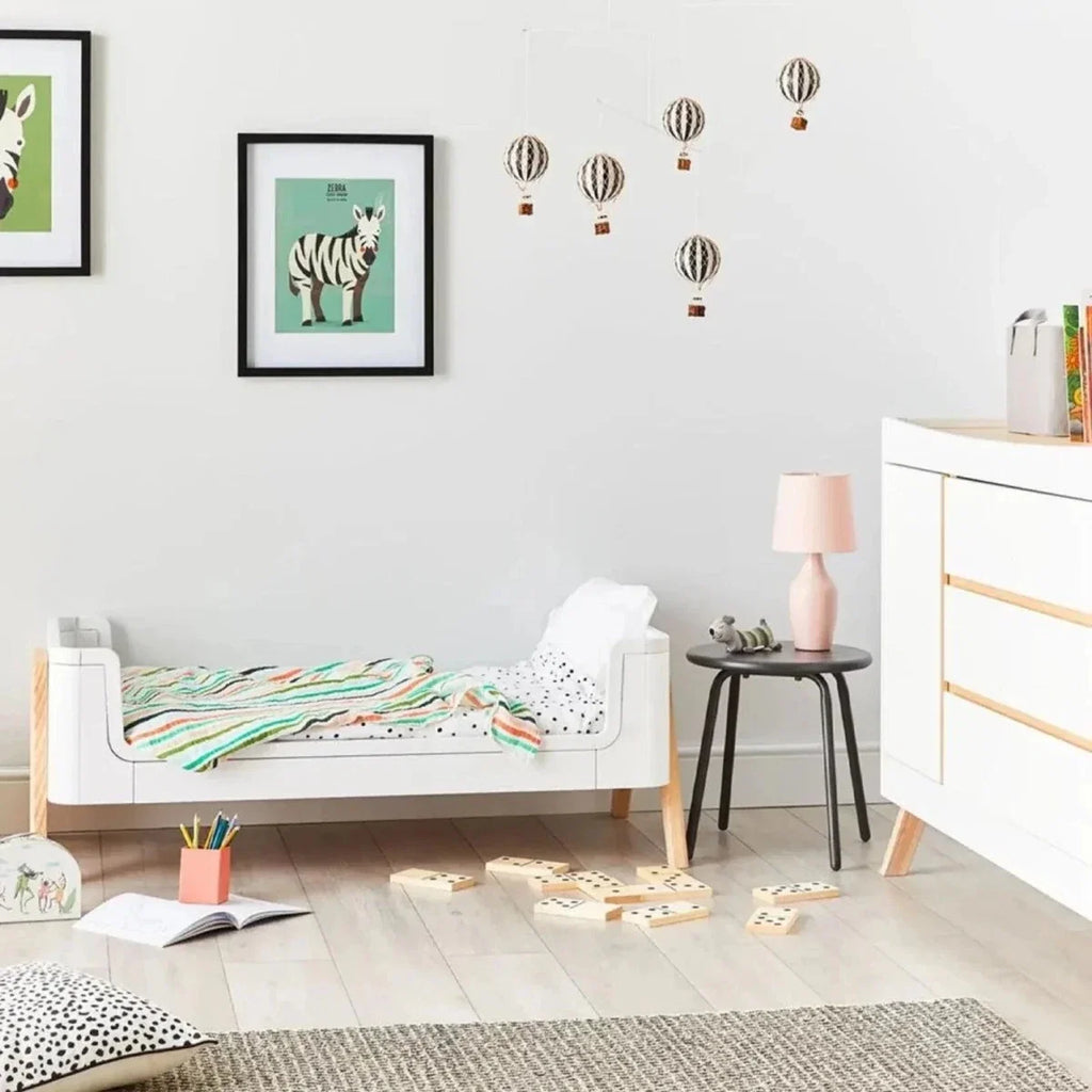 White junior bed extension with padded mattress, raised side rails and light wood legs