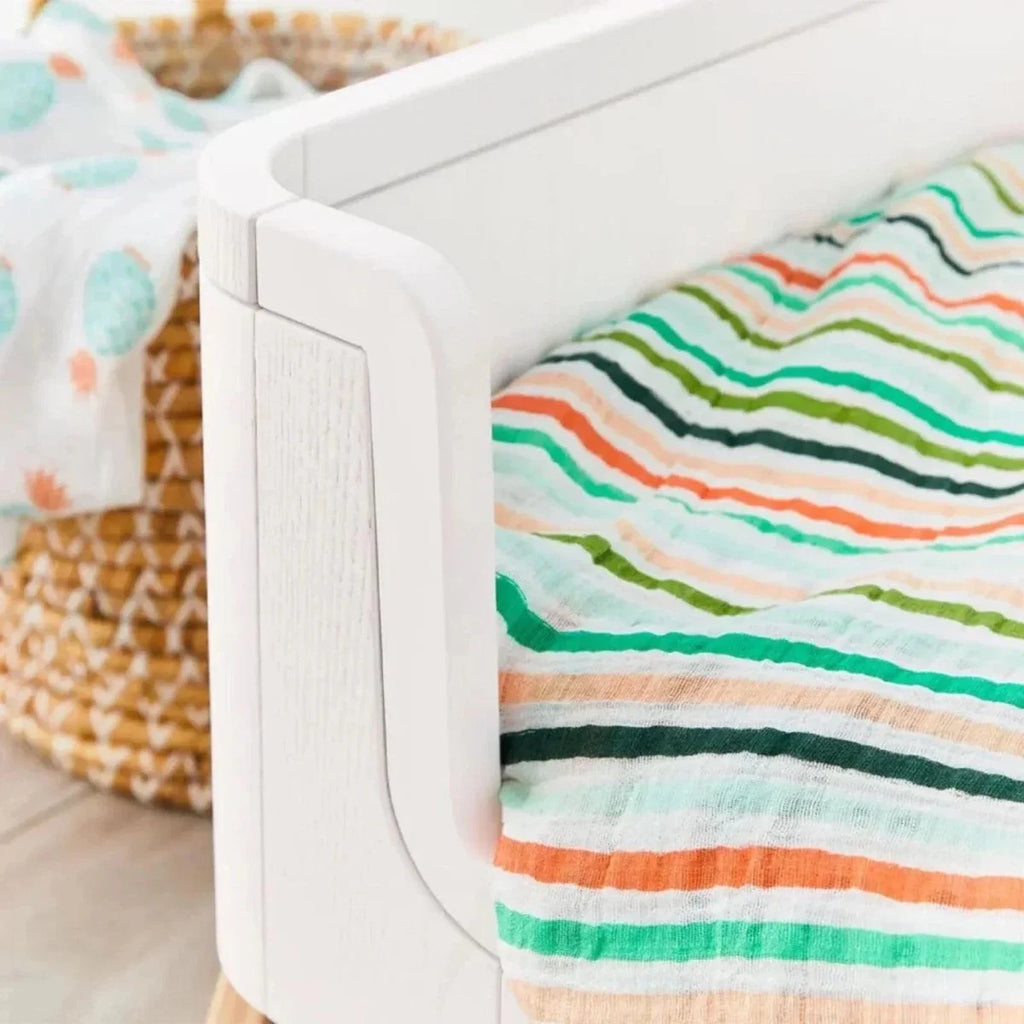 White curved side rail of junior bed extension with striped bedding on padded mattress