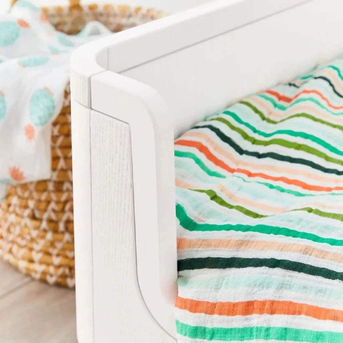 White curved bed rail with natural wood post and colorful striped blanket