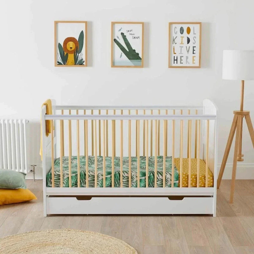 White cot bed with natural wood slats and under-drawer storage, styled in a nursery