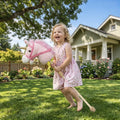 Pink plush unicorn stick horse with gold horn, kid playing in yard