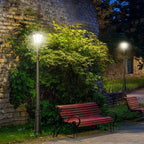 Black solar lamp post light with lantern head glowing along a garden walkway