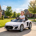 White open-top kids electric car with steering wheel, child smiling outdoors on driveway