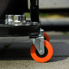 Orange caster wheel under black rolling stool frame for smooth workshop mobility