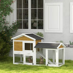 Yellow double-tier rabbit hutch with ramp and dark roof, shown outdoors near house wall