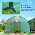 Green walk-in polytunnel greenhouse standing in yard with anchored base