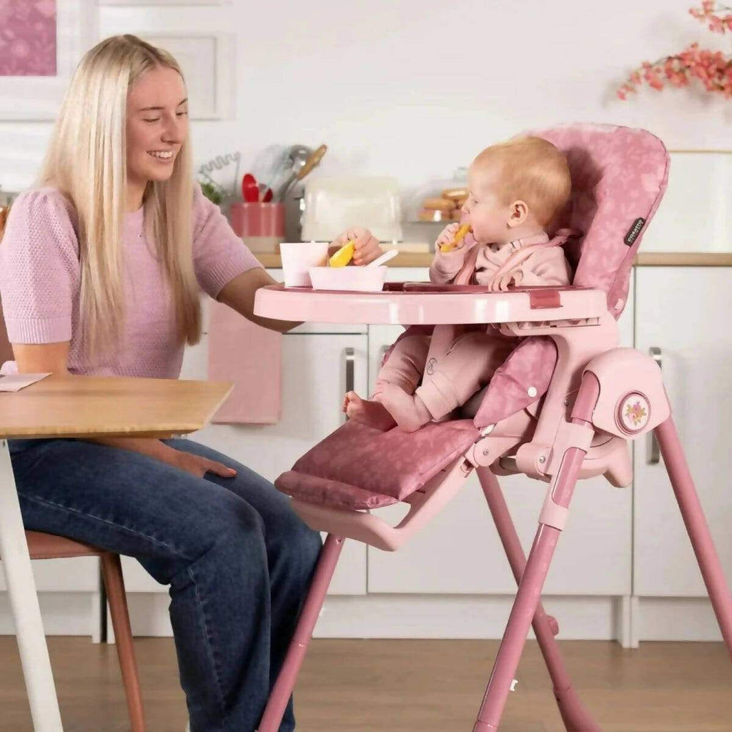 Pink patterned 0+ highchair with tray, baby seated and caregiver nearby