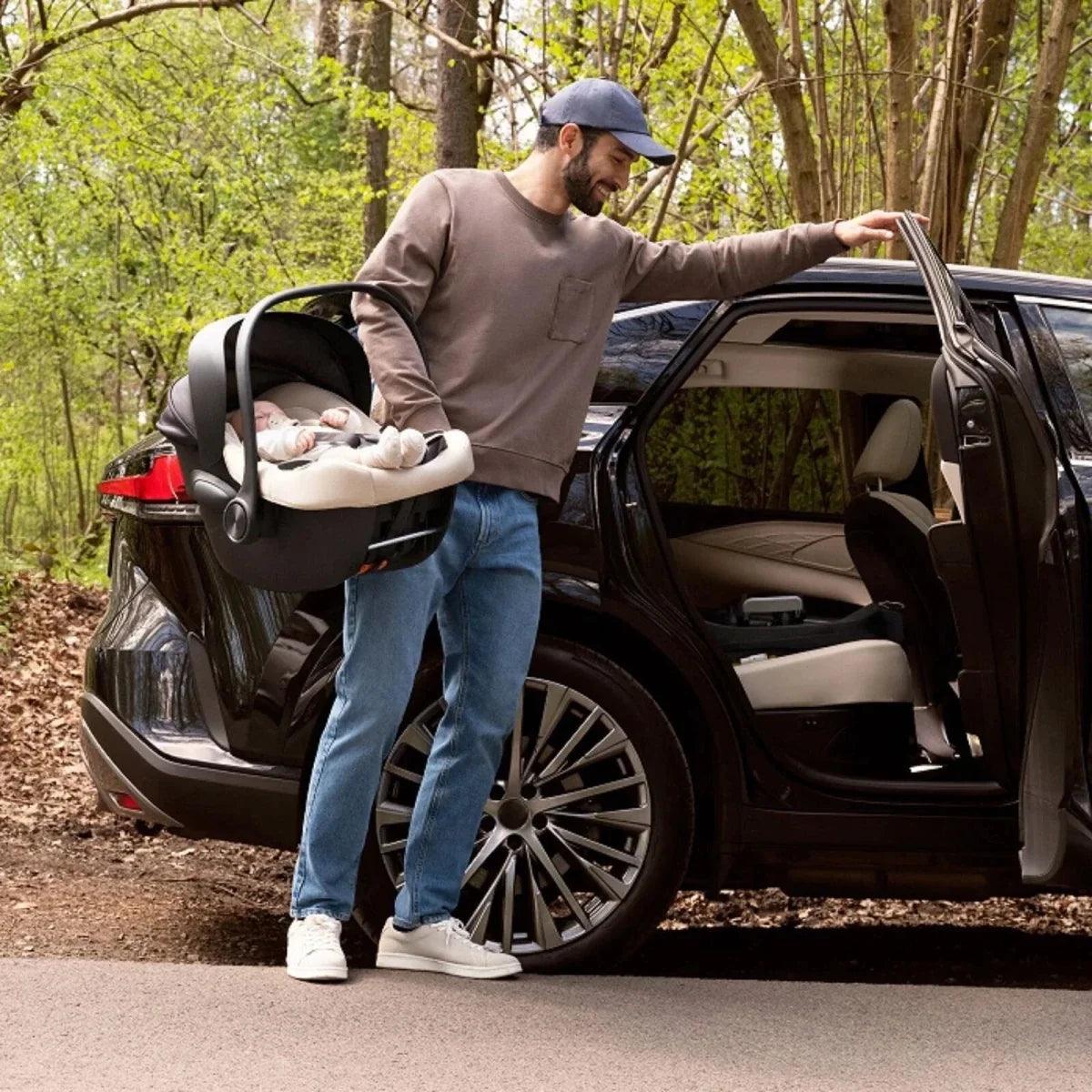 Adult carrying grey modular infant seat outside an open car door with child inside