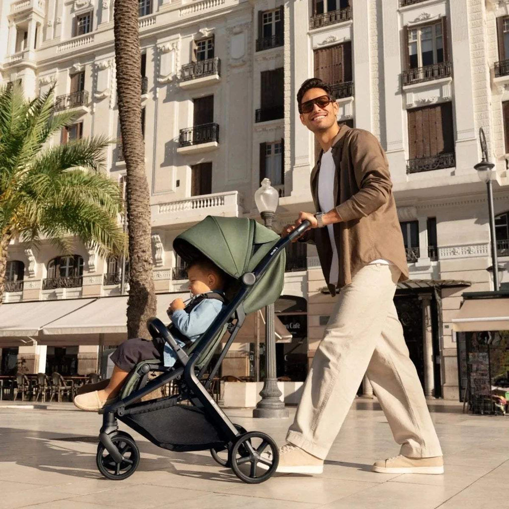 Compact baby stroller in dark green with front wheels and canopy, street side view