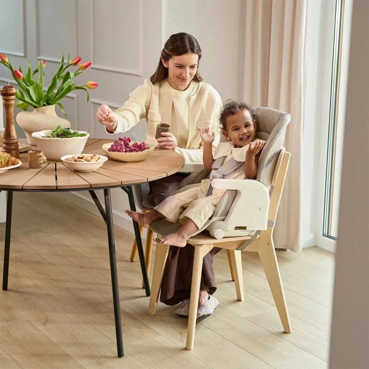 Light-colored 3-in-1 high chair with padded seat, harness, and tray on dining table