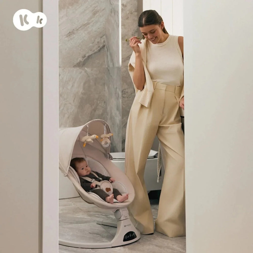Grey baby swing in use with seated baby on an indoor floor