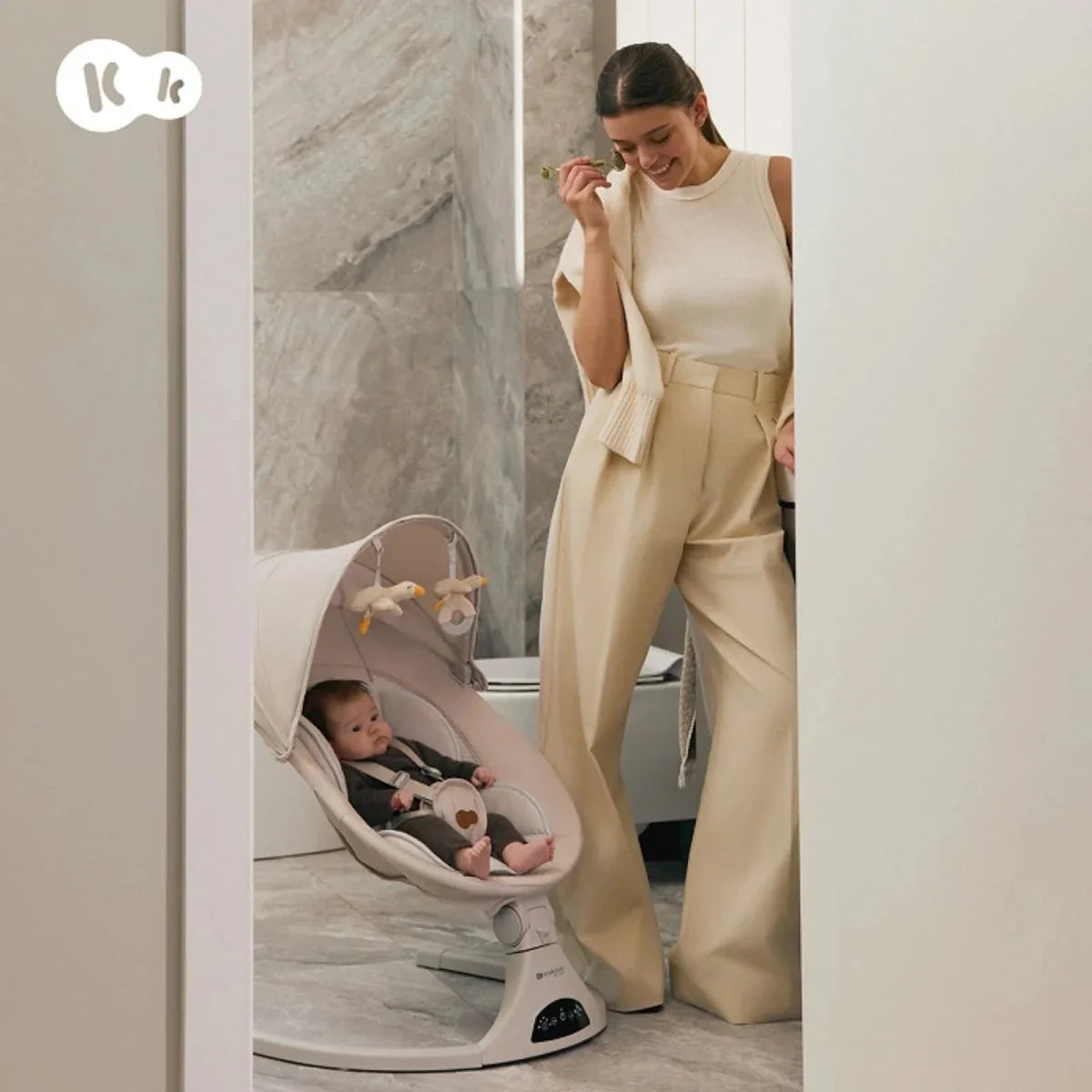 Grey baby swing in use with seated baby on an indoor floor