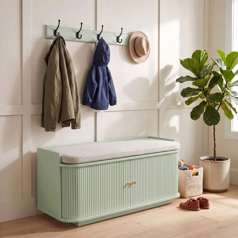 Light green shoe cabinet with cushioned top and wall coat hooks holding bags
