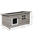 Grey wooden elevated outdoor cat house with two front windows and asphalt roof