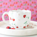 Scalloped white ceramic mug with red cherry and heart print, curved handle