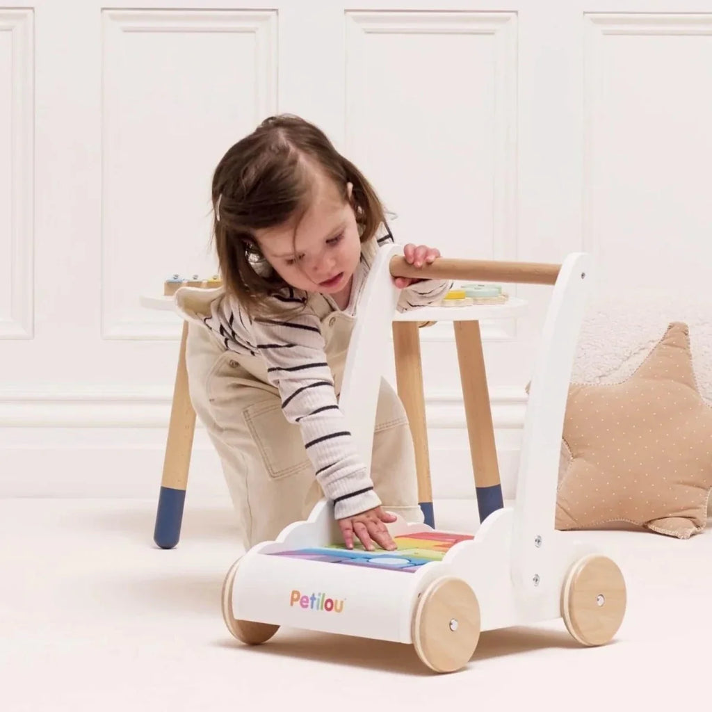 Child using a white wooden block walker with multicolored shape tray