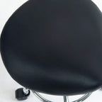 Black cushioned saddle seat with textured upholstery on rolling stool base