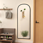 Black arched full-length standing mirror mounted upright against a wall