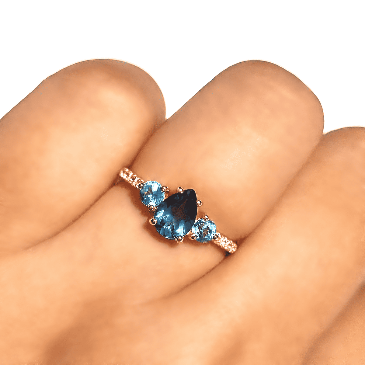 Blue gemstone ring on finger with three stones in rose-gold setting