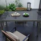 Grey glass-top aluminium table on patio with chairs and small tableware