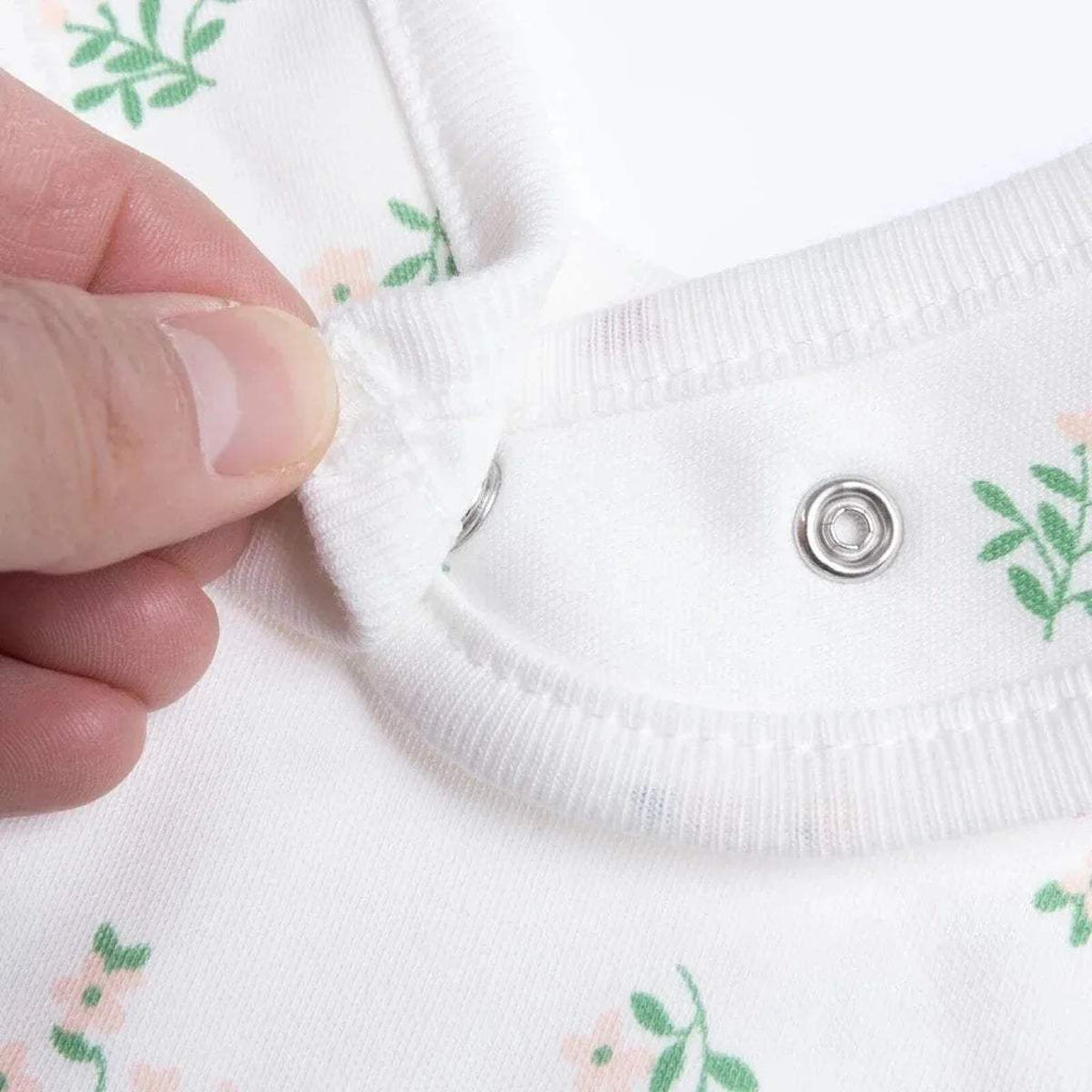 White baby bib close-up showing metal snap and green floral print on the edge.