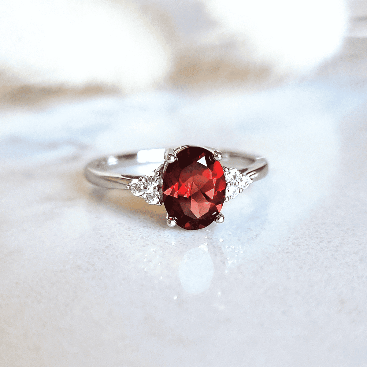Sterling silver garnet ring featuring an oval red garnet center and sparking side accents