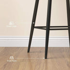 Close-up of black steel legs and footrest on a brown velvet-look bar stool