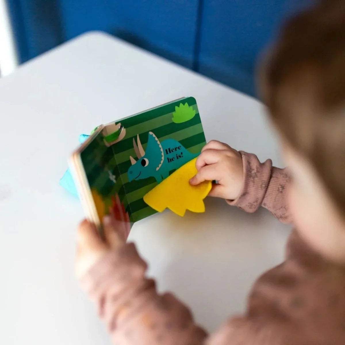 Board book page with green dinosaur illustration and yellow paper flap