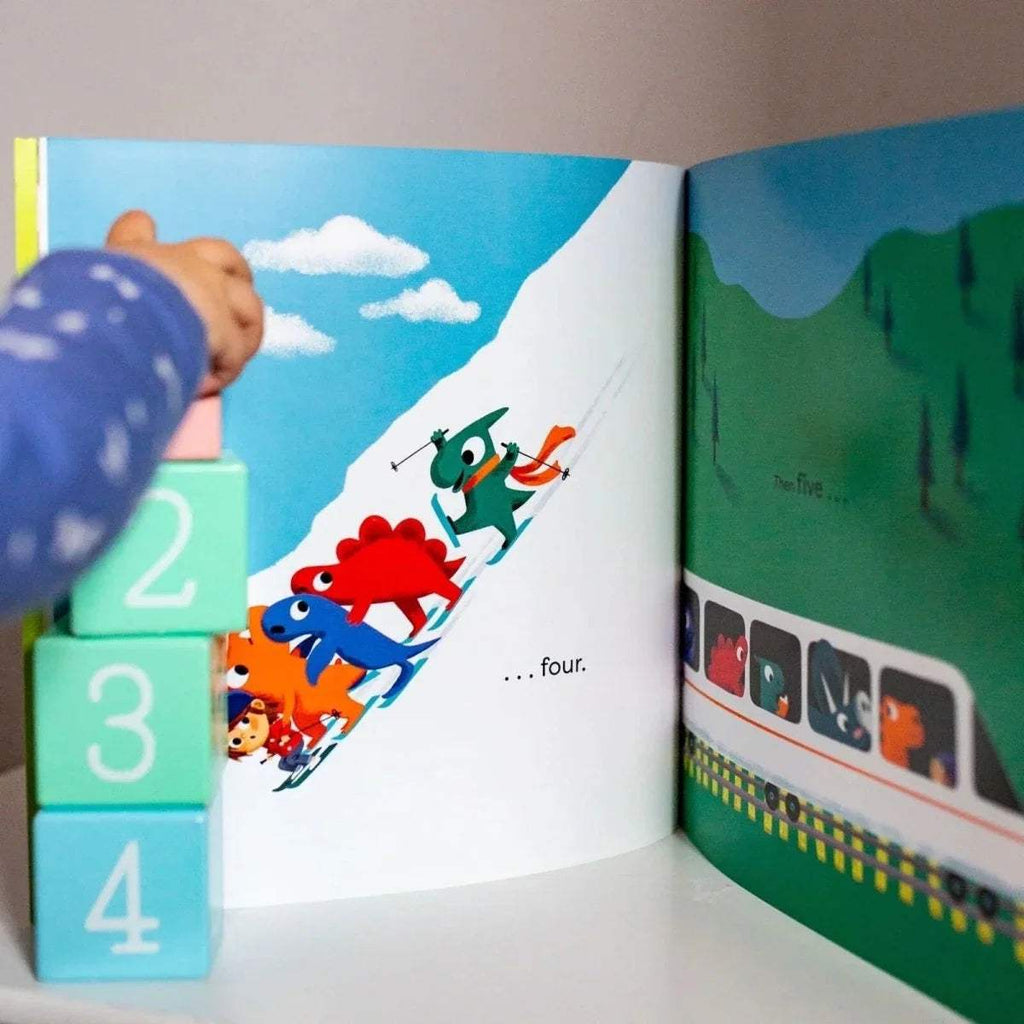 Open dinosaur picture book spread with cartoon dinos, numbers, and numbered cubes