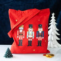 Red nutcracker print tote bag with three toy soldier figures and star accents