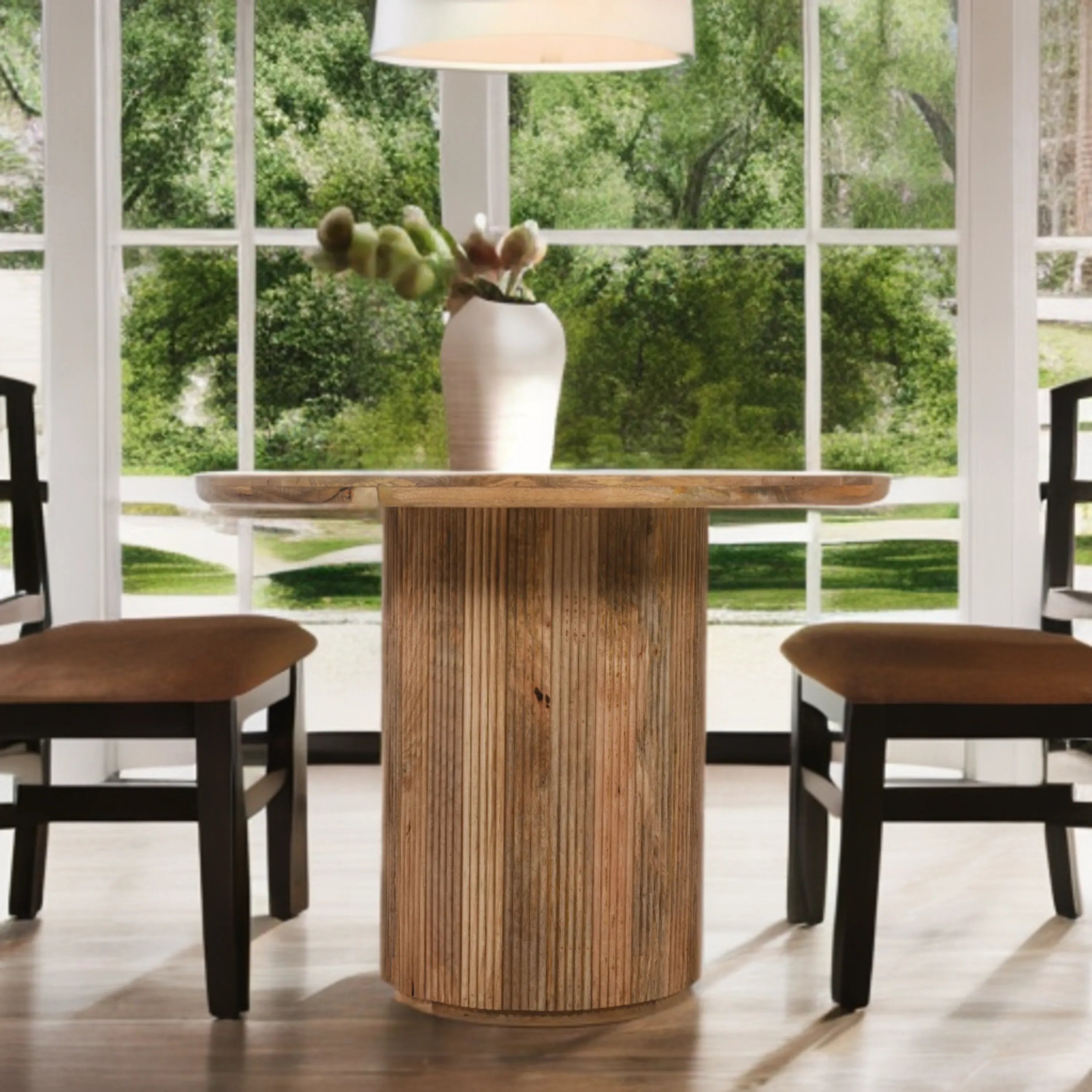 Wooden dining table with a vase of flowers in a room with large windows showing greenery outside.