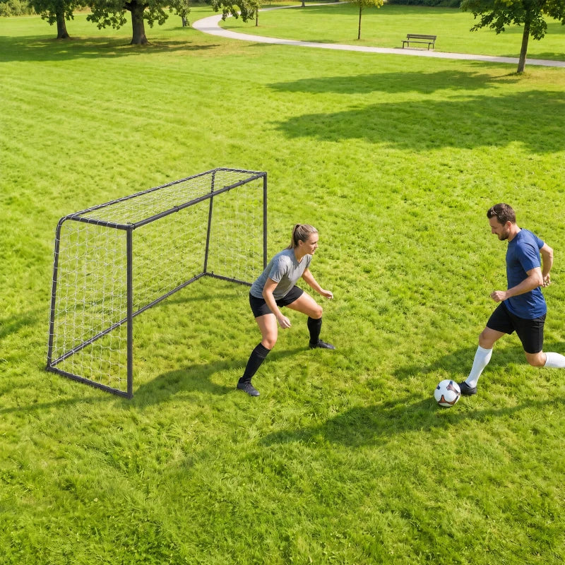Black football goal with white net on grass, players practicing