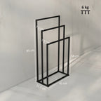Black freestanding towel rack with three bars, side view of open frame.