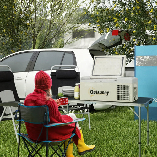 Khaki and grey portable car fridge on a table outdoors, with lid closed and vents