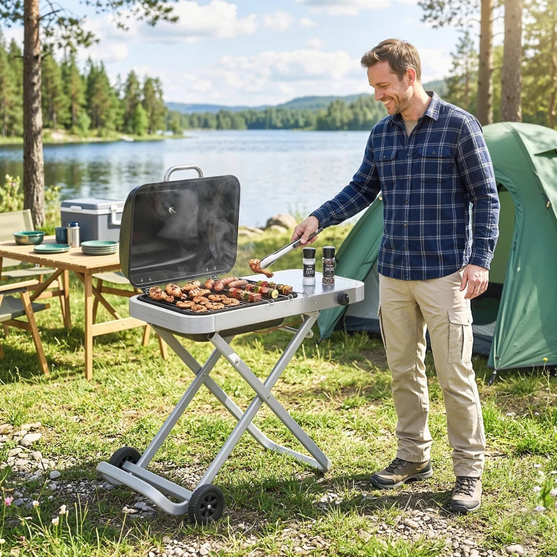 Portable foldable gas grill on wheels beside camping setup, lid open for cooking