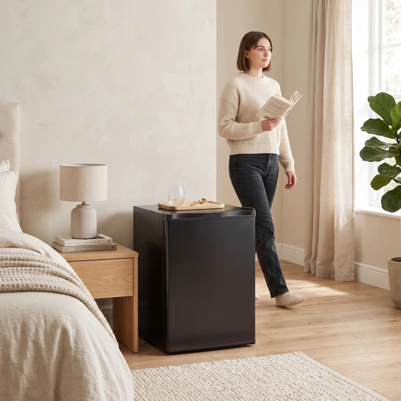 Black mini fridge in a room next to a person standing beside the compact unit.
