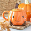 Smiling orange pumpkin mug with fuzzy filling and brown strap on a tray