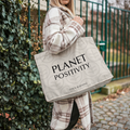 Person holding a tote bag with 'PLANET POSITIVITY' text outdoors.