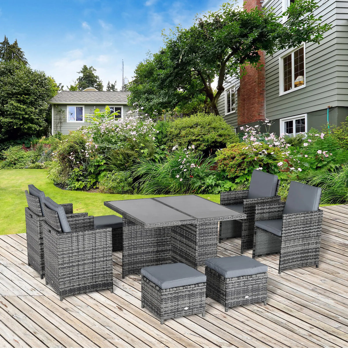 Grey rattan dining set arranged on a patio, with table, chairs, cushions and stools