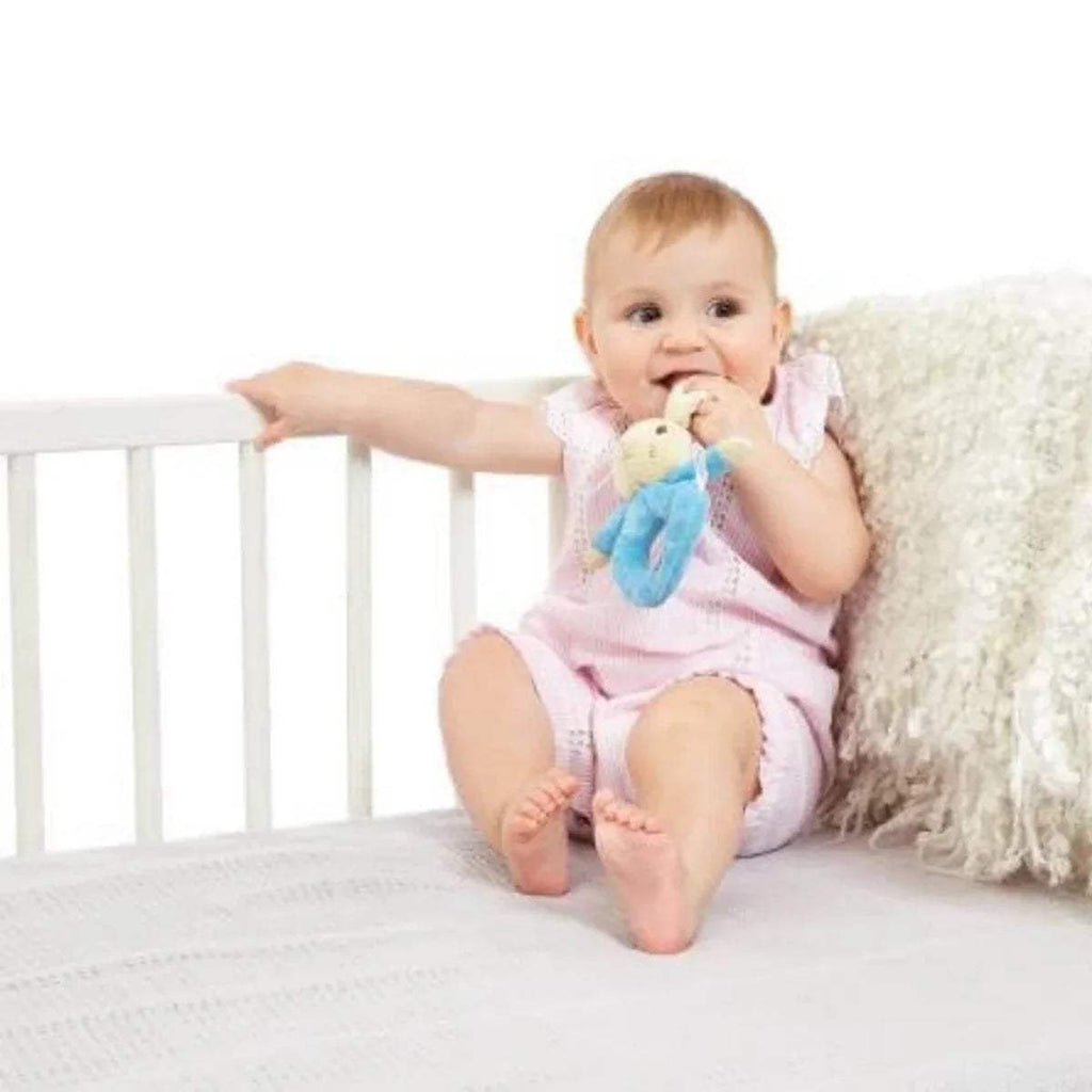 Infant smiling while grasping blue bunny plush ring rattle near face