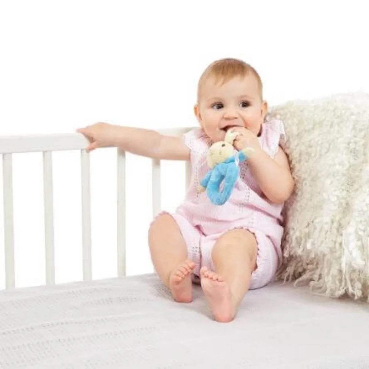 Infant smiling while grasping blue bunny plush ring rattle near face