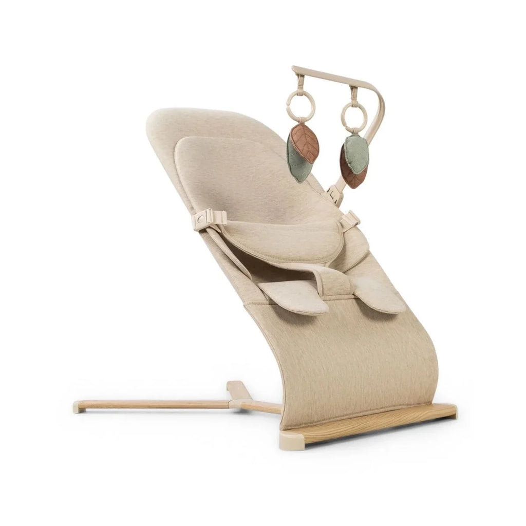Oatmeal baby bouncer with angled legs, reclined seat cushion, and hanging leaf toy arches