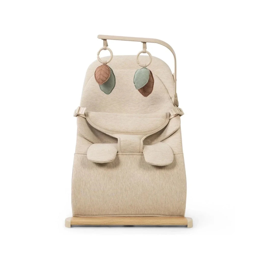 Oatmeal baby bouncer with front view harness pads, two hanging leaf toys, and wooden stand
