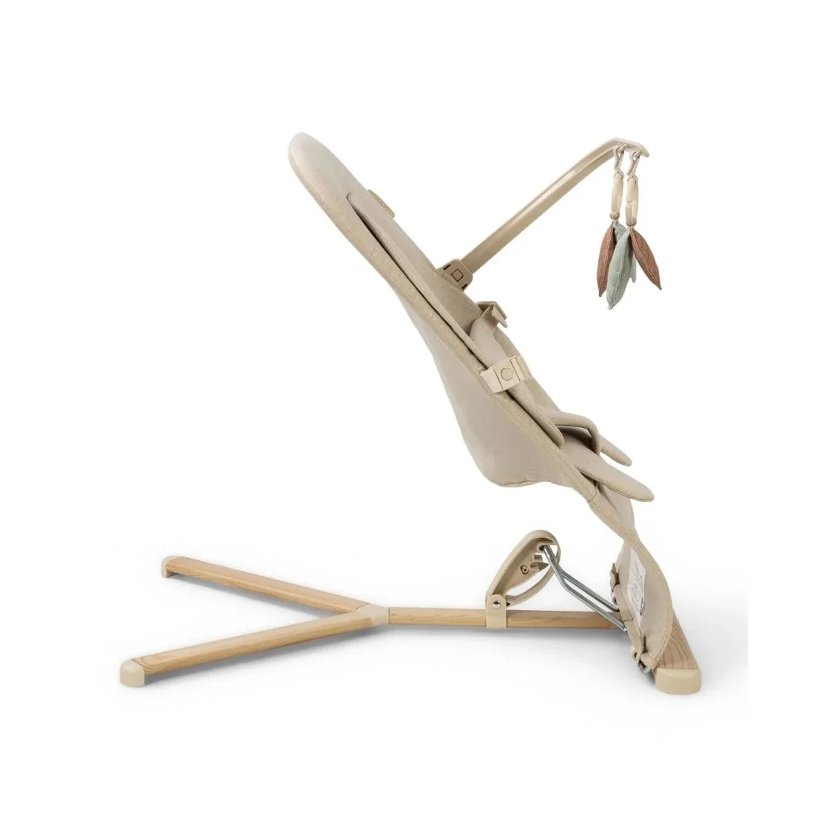 Oatmeal baby bouncer in side view with reclining frame, harness straps, and leaf toy bar