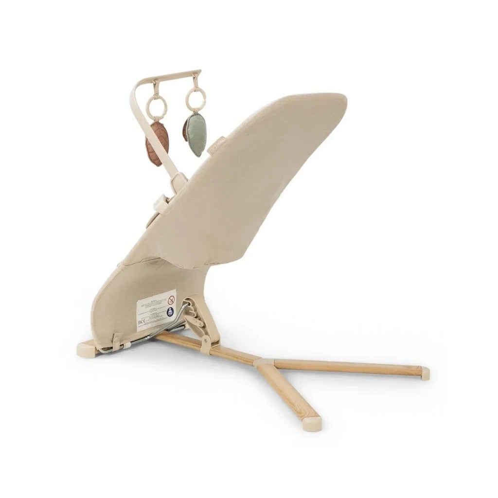 Oatmeal baby bouncer angled side view with hanging leaf toys and reclining wooden frame