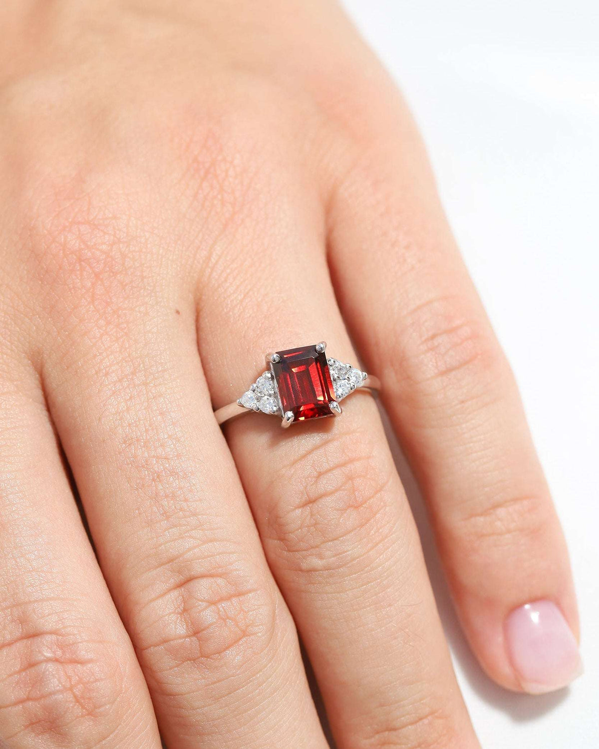 Silver ring featuring a red emerald-cut center stone with clear stone accents